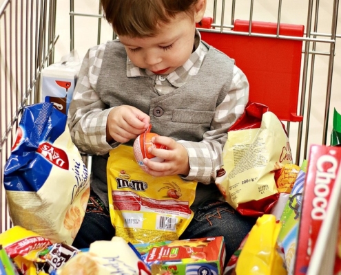 boy-in-supermarket-trolley-surrounded-by-bright-food-packaging